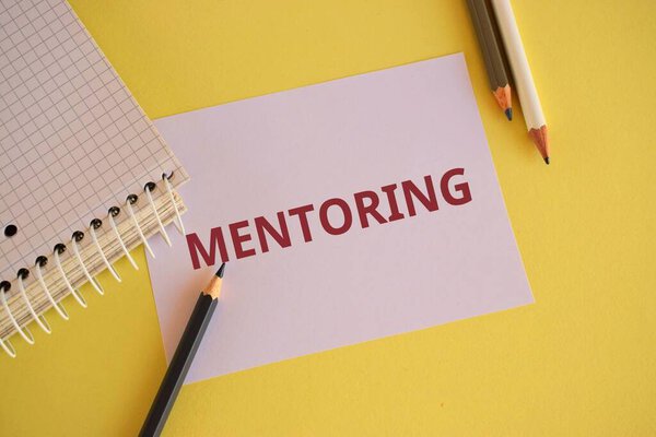 White paper with red text MENTORING on yellow background. Word writing text Mentoring. Business concept for To give advice or support to a younger less experienced person.