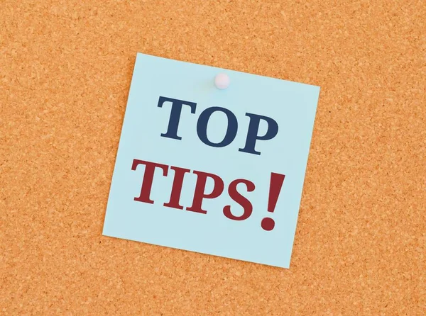 Handwriting text writing Top Tips. Concept meaning small but particularly useful piece of practical advicese Top Tips in blue and red text on an index card pinned to a cork notice board as a reminder.