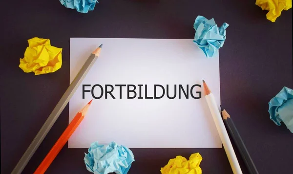 Fortbildung written on a white paper . German Language means further education. Pencils and paper lobs on dark backdrop