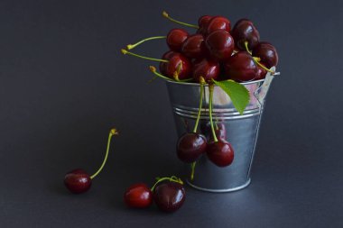 Kırmızı kirazlar koyu arkaplanda metal bir kovanın içinde kapanıyor. Yaz tadı. Taze böğürtlen suyun altında.