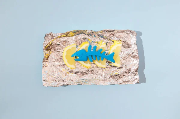 Alüminyum folyoda plastik mavi bir balık ve limon. Yaratıcı yaz yemekleri konsepti. Asgari çağdaş tasarım.