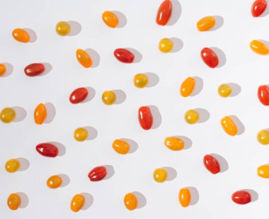 A cute pattern or wallpaper made of red, orange and yellow cherry tomatoes on a white background. Happy summer food or summer vibes concept.
