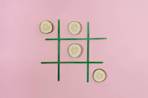 A tic tac toe game with cucumbers on a pastel pink background. Minimal creative summer holidays design.