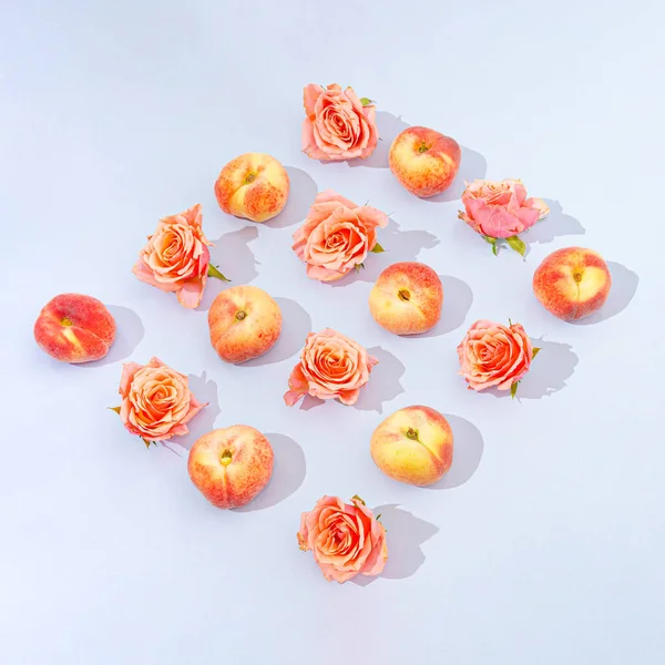 A lovely pattern made of peaches and roses on a pastel blue background. Summer fruits and flowers concept. Festive design. Flat lay