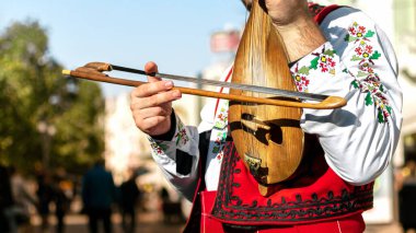 Bulgar folk müzisyeni - geleneksel ulusal kostümlü kemancı - Bulgaristan 'ın Filibe kenti sokaklarında eski bir telli enstrüman çalıyor - gadulka. Bulgar folkloru ve kültürü. Sokak sanatçısı