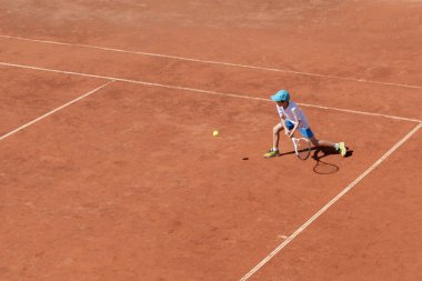 Açık tenis kortunda tenis oynayan bir çocuk. Çocuk konsantre olmuş ve oyuna odaklanmış. Bireysel spor. Kararlı genç bir atlet. Çocuklar turnuvası, maç. Aktif spor.