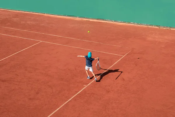 子供テニスのスポーツコンセプト 子供テニス選手は赤土コートでサービスを行います 少年運動選手 上からの高いビュー コピースペース — ストック写真