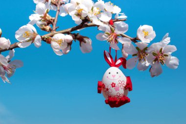 Tavşan gibi süslenmiş komik bir paskalya yumurtası bir ağacın çiçek açan dalına asılır ve arka planda mavi gökyüzü. Mutlu Paskalyalar. Kutlama dekorasyonu, tebrik kartı. Metin için boşluk.