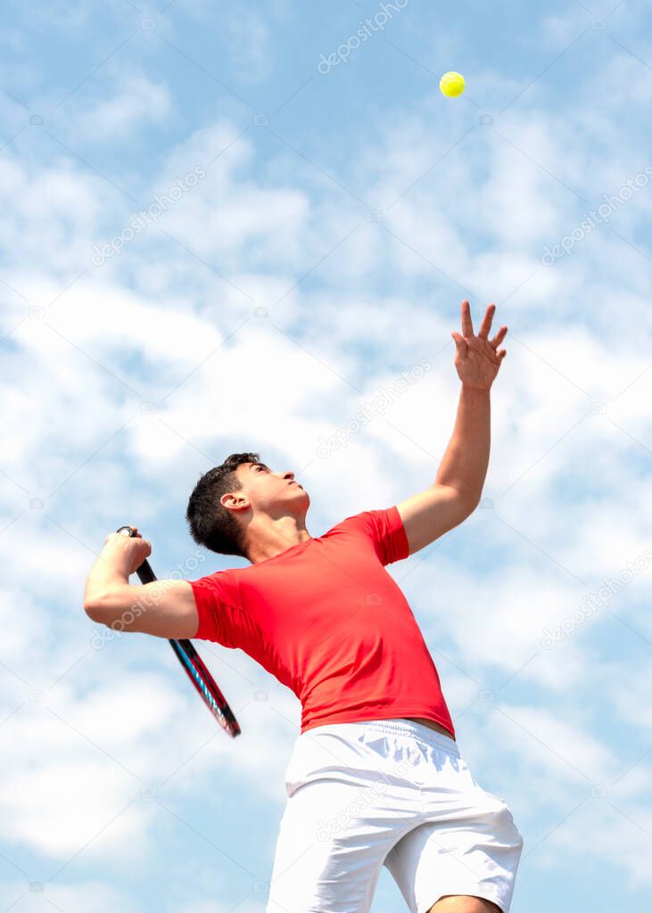 Cute male tennis player athlete in action. Young tennis player teen with racket hits flying ball in jump and blue sky background. Competitive sports game, match. Vertical banner Copy space