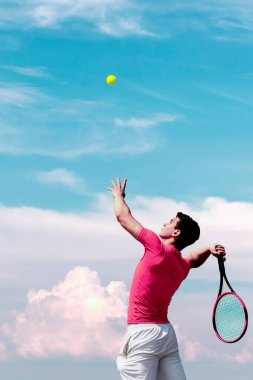 Raketi olan genç tenisçi zıplayarak uçan topa ve mavi gökyüzüne vuruyor. Şirin erkek tenis oyuncusu iş başında. Rekabetçi spor aktif oyun, maç. Dikey afiş Boşluğu Kopyala