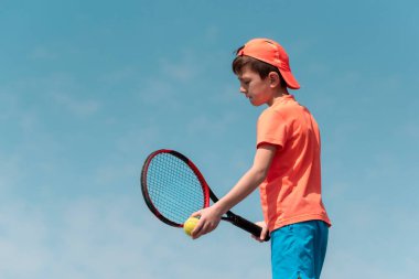 Çocuklar tenis oyunu konsepti. Çocuk tenisçi elinde topu mavi gökyüzüne karşı tutuyor. Çocuk sporları, aktif yaşam tarzı. Arka plan, Arkaplan, Boşluğu kopyala
