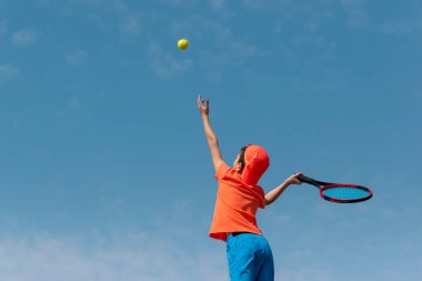 Çocuklar tenis oyunu konsepti. Çocuk tenisçi elinde topu mavi gökyüzüne karşı tutuyor. Çocuk sporları, aktif yaşam tarzı. Arka plan, Arkaplan, Boşluğu kopyala