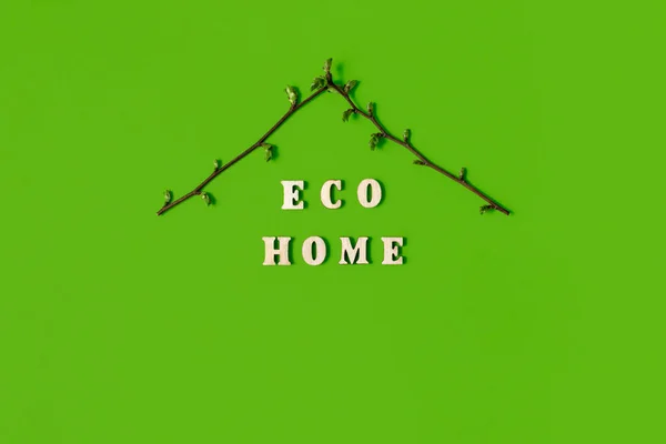 Eco home word and symbolic roof made of spring blossoming twigs on green background. Environmentally green real estate. Eco-friendly family house, care nature and environment. Card or poster