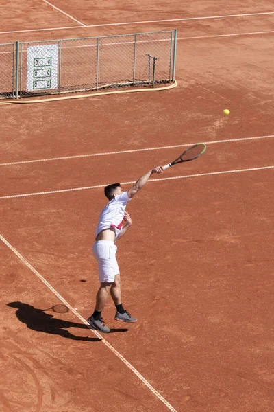 在比赛开始时 年轻的网球选手在橙色粘土球场上发球时跳跃和击球 运动员在比赛中运动 垂直运动背景 复制空间 — 图库照片