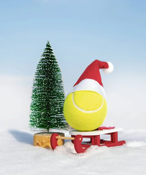 Noel ve yeni yıl kartı yeşil köknar ağacı ve sarı tenis topu ile kırmızı Noel Baba şapkası ve beyaz kar üzerinde kızak. Kış tatili, kutlama konsepti. Spor tenis partisi.