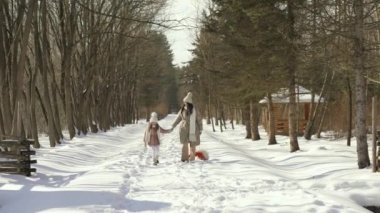 Ön manzara. Anne ve kızı karlı ormanda kapı kolunun yanından yürür.