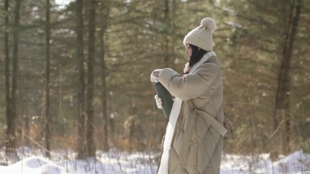 Vista lateral. La chica abre un termo con té en un bosque nevado — Vídeo de stock