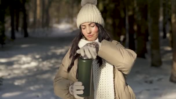 Вид спереди. Девушка открывает термос с чаем в заснеженном лесу — стоковое видео