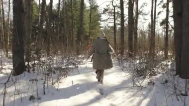 Ağır çekim. Güneş ışığı. Manken karlı bir ormanda yürüyüp poz verir..