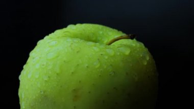 Yeşil elma su damlacıklarıyla yakın plan. Elma siyah bir arkaplanda kendi ekseni etrafında döner. Soyut görüntüler