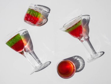 İçinde parlak kırmızı ve yeşil dolgu olan dört kristal bardak uzanır ve ışık arka planına karşı dururlar. Parlak güneş, ilginç gölgeler. Kutlama ve eğlence atmosferi. Lezzetli yaz tatlıları