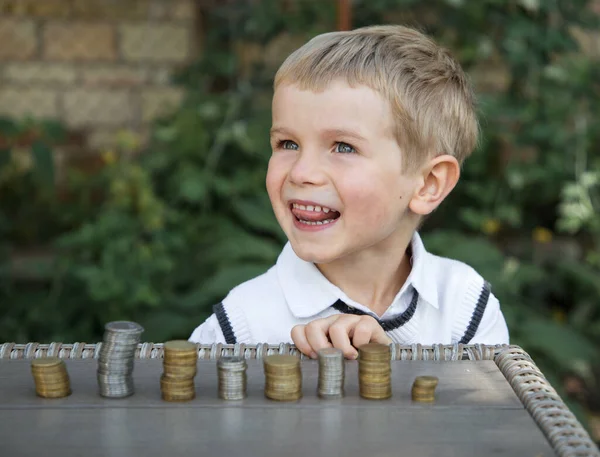 Portrait of a funny little lovely boy who lays out in columns coins on the table. focus on face. Little financier, investment in the future. Child saves money for a dream
