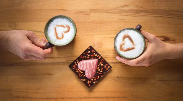 男人和女人的手拿着完全相同的咖啡和牛奶 还有肉桂心 旁边躺着一颗美丽的巧克力心 纹理米色木制背景 爱情的概念 — 图库照片