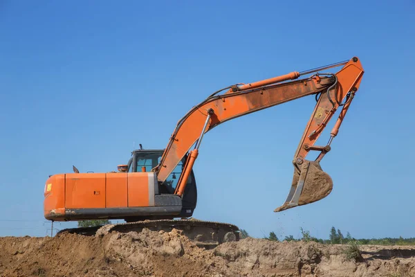 huge orange crawler excavator at work on earthen mountain in a sand quarry, on a sunny day against a blue sky. View from below