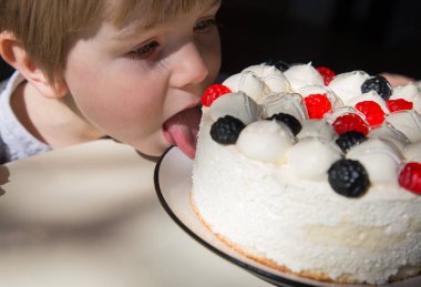 Doğum günü çocuğu sessizce diliyle lezzetli pastadaki kremayı yalıyor. Lezzetli tatlı. Şenlik partisi. seçici odak
