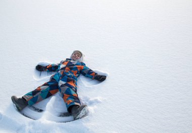 Kış üniformalı neşeli çocuk karda uzanıyor, elini aşağı yukarı hareket ettiriyor, dışarıda oynuyor, kışın tadını çıkarıyor. Karda bir çocuk meleklerin figürlerini gösteriyor.