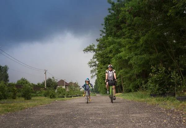 boy of 4 years old and man on bicycles are driving fast along road, in hurry to get away from thundercloud. Active healthy lifestyle. Be like dad. Family pastime, daddy and son bike ride