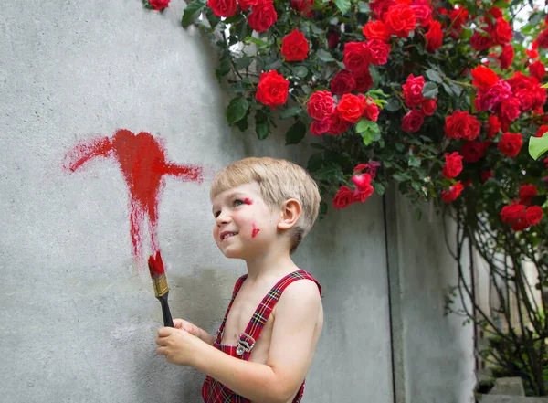 Lindo Niño Overoles Dibuja Corazón Con Pintura Roja Una Valla — Foto de Stock
