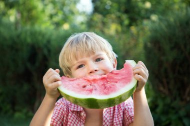 İştahlı tatlı çocuk büyük bir parça karpuz yiyor. Lezzetli yaz meyvesi.