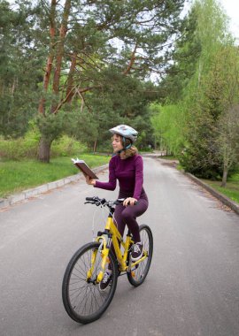 Kasklı güzel kız bisiklete biniyor ve coşkuyla kitap okuyor. Okuma ve bisiklete binme hobisini birleştir. Dijital detoks