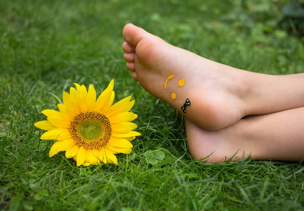 Uśmiech Narysowany Jest Gołych Stopach Dziecka Leżącego Trawie Żółty Słonecznik — Zdjęcie stockowe
