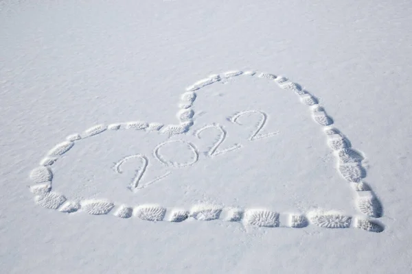 symbolic drawing of heart in the snow, made by shoe prints. Inside heart are numbers 2022. Footprints in the snow. Christmas Eve walking fun, winter holidays
