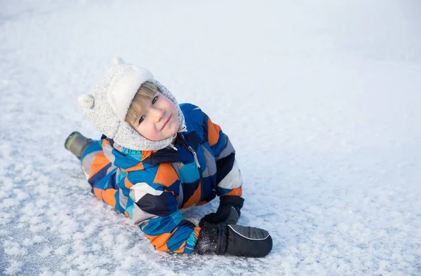 4-5 yaşlarında, kışın giydiği tulumlu sevimli bir çocuk karlı zeminde oturuyor. Çocuklarla karda aktif kış yürüyüşleri. Mevsimlik sevinçler, mutlu çocukluk. Soğuk hava..