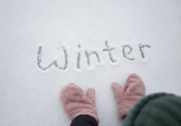 雪に書かれた冬の言葉とピンクのふわふわのミトンで女性の手 こんにちは冬 — ストック写真