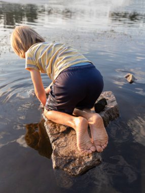 9 yaşındaki çıplak ayaklı bir çocuk kayanın üzerinde kambur bir şekilde oturur, nehir kıyısındaki suya bakar ve doğayı gözlemler. İlginç bir çocukluk dönemi, açık havada oynamak hafta sonlarını deniz yaşamını çalışarak geçirmek. Yaşam biçimi.
