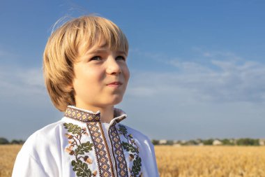 Altın buğday tarlasına ve mavi gökyüzüne karşı geleneksel Ukrayna işlemeli gömlek giyen 10 yaşındaki bir çocuğun portresi. Ukrayna 'nın gerçek çocukları. Vatansever eğitim. Bağımsızlık Günü