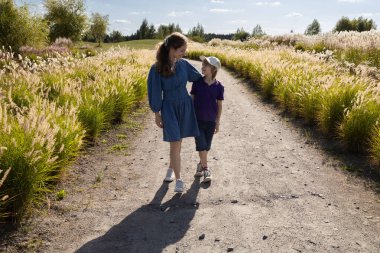 İki çocuk, bir abla ve bir erkek kardeş güneşli bir günde parkta gezinirken mutlu bir şekilde sohbet ediyorlar. Arkadaş canlısı aile ilişkileri. Kardeş desteği.