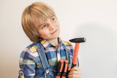 Çekiç ve tornavidayla ekose gömlekli bir çocuğun pozitif portresi. Aletleri kullanmayı ve babasına tamirat işlerinde yardım etmeyi öğreniyor. Ev onarımında küçük bir yardımcı..
