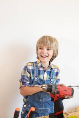 Kablosuz matkap ve tornavidayla ekose gömlekli neşeli bir çocuk. Bir çocuk aletleri kullanmayı ve kendi elleriyle bir şeyler yapmayı öğrenir. Ev onarımında küçük bir yardımcı.