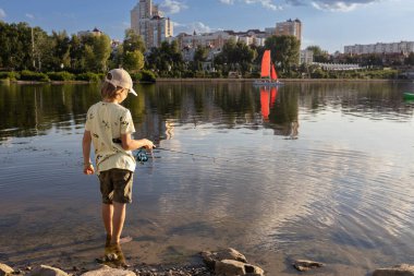 Çocuk nehir kıyısında suyun içinde dururken bir oltayla balık yakalıyor. Güzel manzara. Bir çocuk için en sevdiği hobi. balık tatili