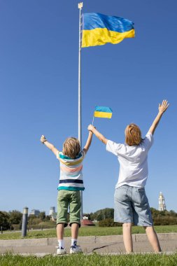 Çocuk ve kadın, Kyiv 'de büyük, yüksek bir bayrağın önünde duruyor, mavi Ukrayna bayrağıyla el ele tutuşuyorlar. Aile, mülteciler, birlik, destek, vatanseverlik. Ukraynalılar savaşa karşı. Ukrayna 'yı Destekle