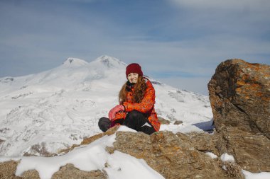 Karlı dağ zirvesinde bir uçurumda oturan genç bir kadın görüntüsü 