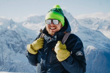 Karlı dağ zirvesinde bir uçurumun kenarında duran genç bir adam görüntüsü 