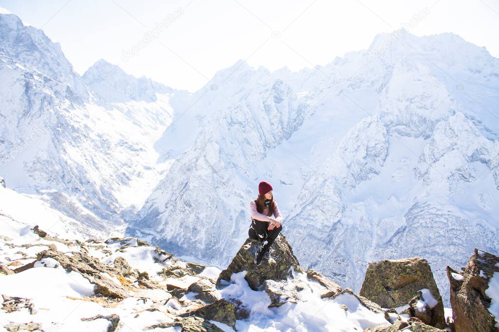View of a young woman sitting on a cliff by snowy mountain peak 