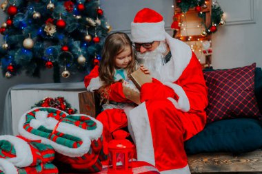 Noel Baba, Noel ağacının önünde güzel bir kızla hediye açıyor. 