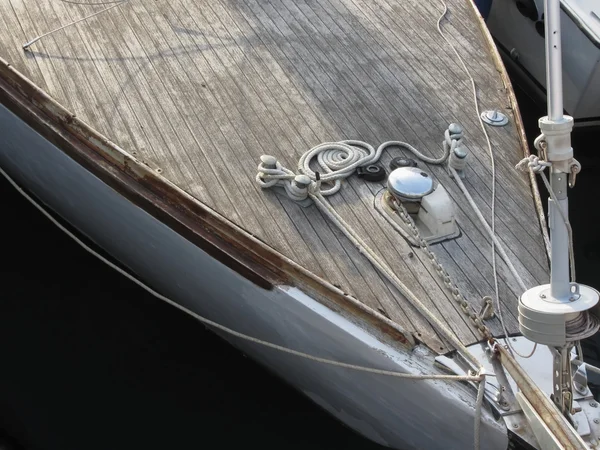 Prow of sailboat moored in the harbor with wooden deck in foreground — Stock Photo, Image